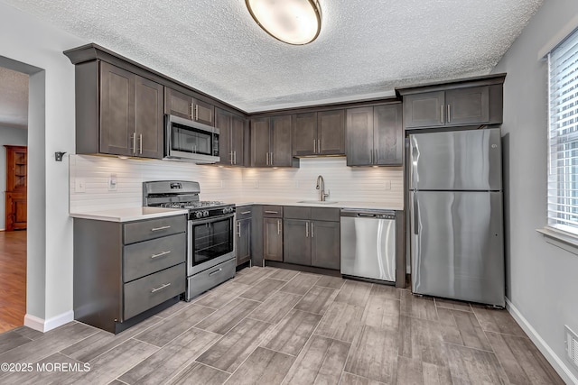 kitchen with appliances with stainless steel finishes, a sink, light wood-style flooring, light countertops, and a textured ceiling
