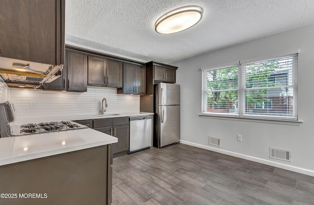 kitchen featuring appliances with stainless steel finishes, a textured ceiling, light countertops, dark brown cabinets, and a sink