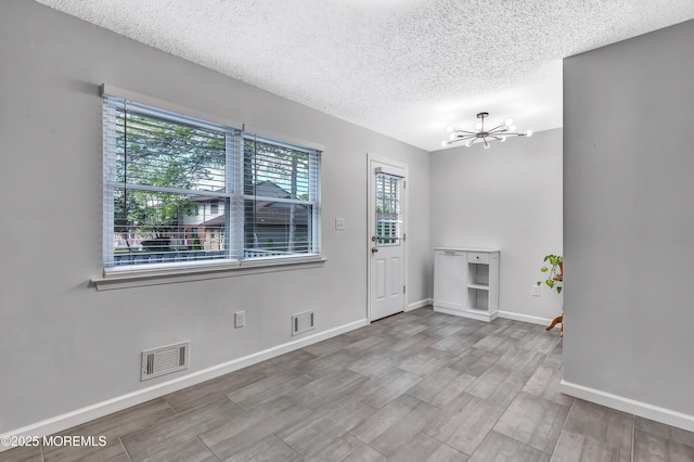 entryway with a textured ceiling, a chandelier, wood finished floors, and baseboards