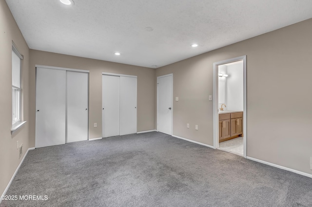 unfurnished bedroom featuring two closets, recessed lighting, carpet, a sink, and baseboards