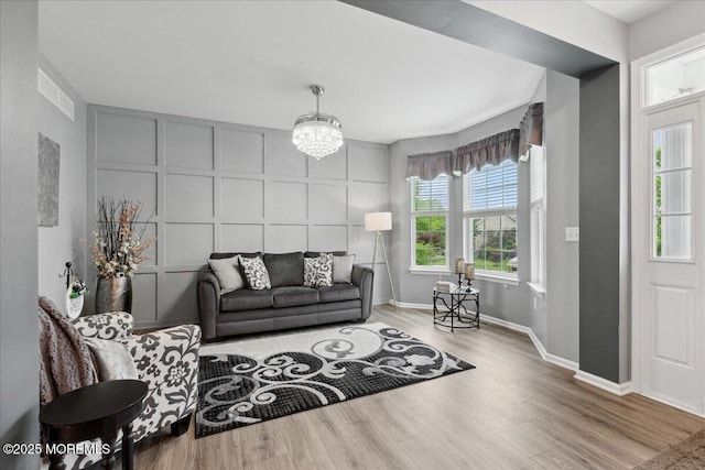 living room with a decorative wall, wood finished floors, a chandelier, and baseboards