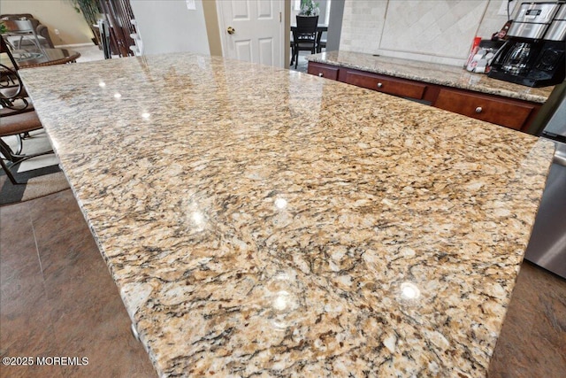 kitchen featuring light stone countertops, decorative backsplash, brown cabinets, and a breakfast bar