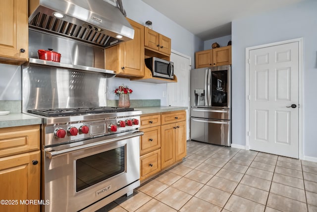 kitchen featuring appliances with stainless steel finishes, wall chimney range hood, light countertops, light tile patterned floors, and baseboards