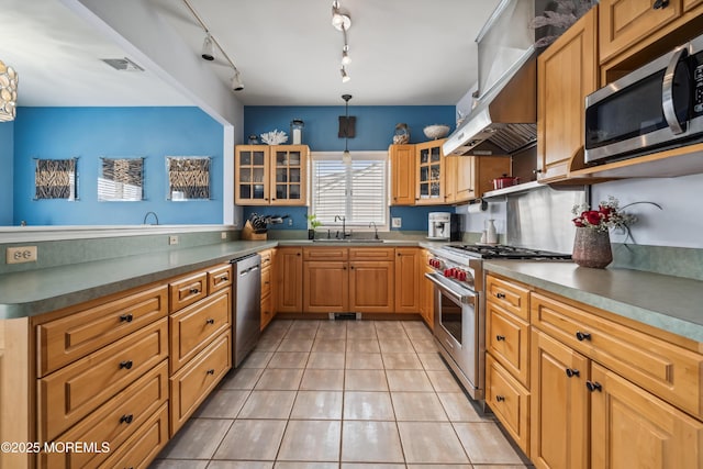 kitchen with appliances with stainless steel finishes, a sink, a peninsula, light tile patterned floors, and glass insert cabinets
