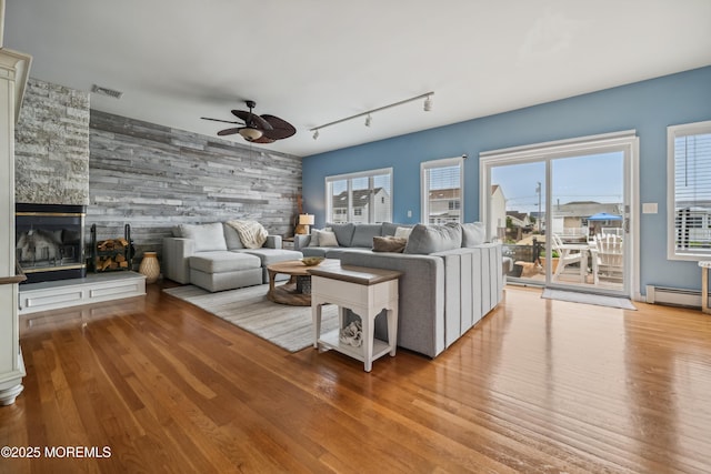 living room with a ceiling fan, wood finished floors, track lighting, baseboard heating, and an accent wall