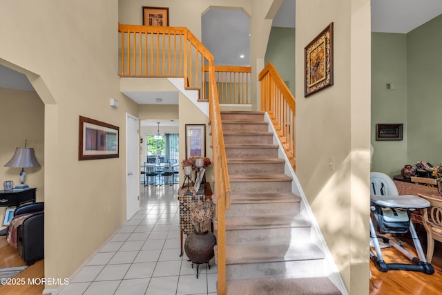 staircase with arched walkways, tile patterned floors, and a towering ceiling