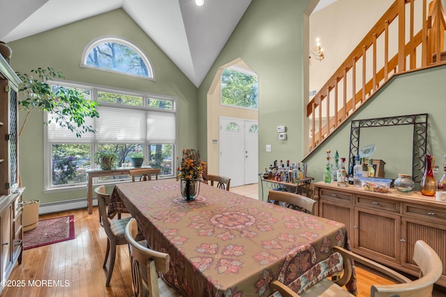 dining area featuring high vaulted ceiling, a baseboard heating unit, light wood finished floors, and stairs
