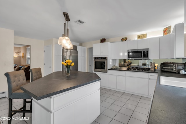 kitchen with stainless steel appliances, dark countertops, light tile patterned floors, a kitchen island, and a sink