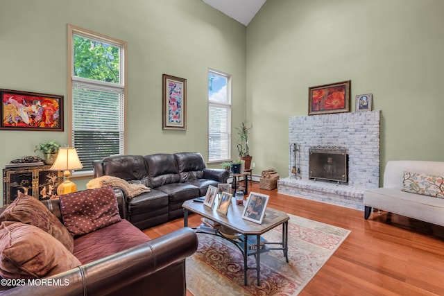 living room with healthy amount of natural light, high vaulted ceiling, wood finished floors, a brick fireplace, and baseboard heating