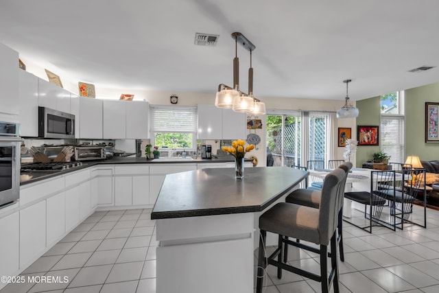 kitchen with dark countertops, stainless steel appliances, a kitchen breakfast bar, and light tile patterned floors