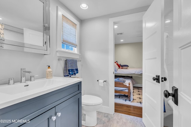 ensuite bathroom with toilet, wood finished floors, vanity, and recessed lighting
