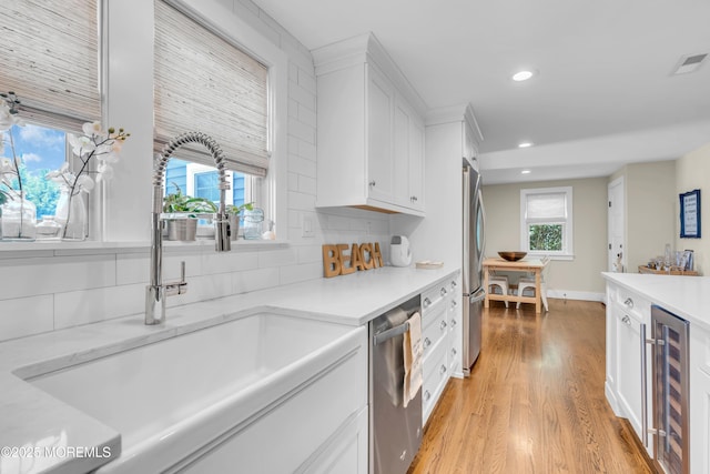 kitchen featuring stainless steel appliances, beverage cooler, a sink, recessed lighting, and white cabinetry