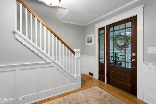 foyer entrance with ornamental molding, wood finished floors, stairway, a decorative wall, and wainscoting
