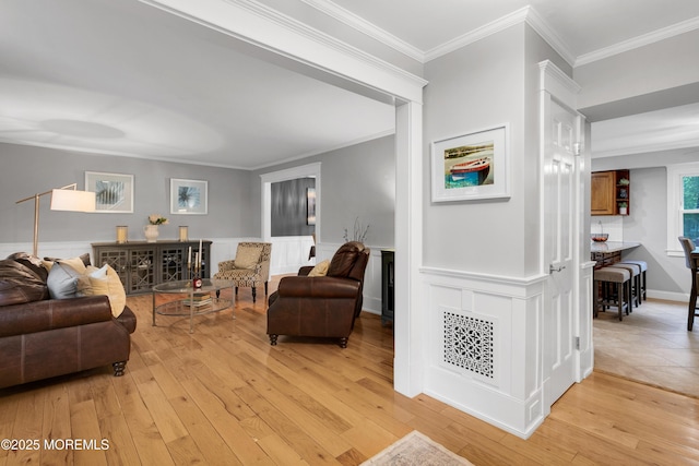 living area with light wood-style floors, crown molding, and a wainscoted wall