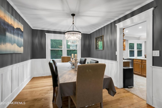 dining room with crown molding, a chandelier, wainscoting, light wood-style floors, and a decorative wall