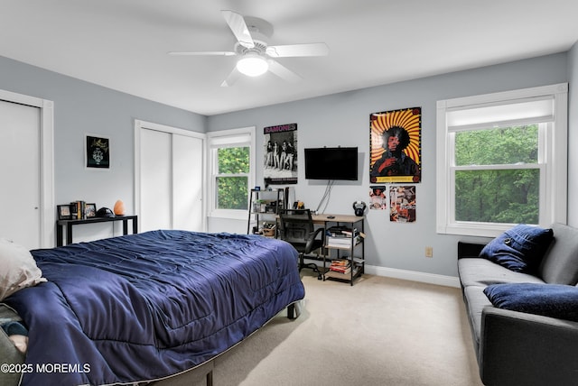 carpeted bedroom featuring baseboards, two closets, a ceiling fan, and a desk