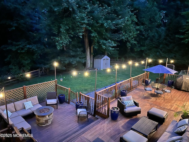 deck at twilight featuring outdoor dining area, an outdoor living space with a fire pit, a shed, and an outdoor structure