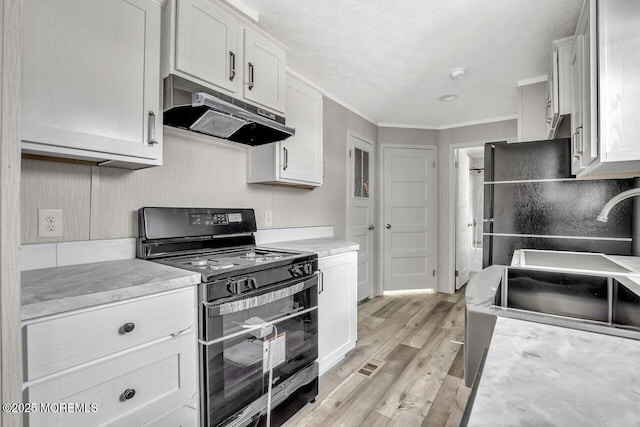 kitchen featuring black gas range, under cabinet range hood, light countertops, light wood-style floors, and ornamental molding