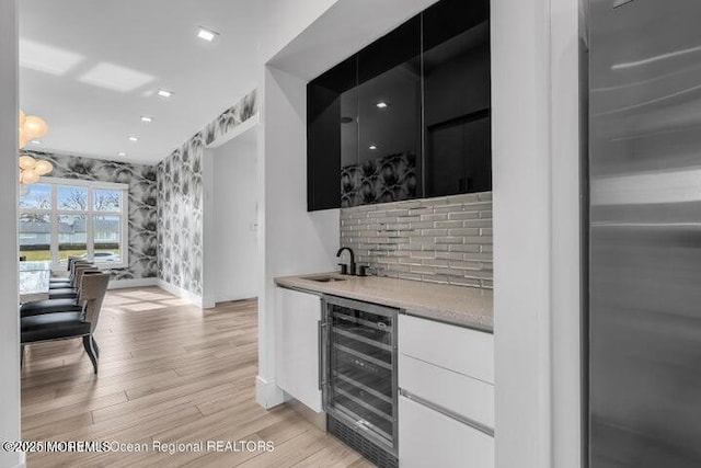 indoor wet bar with wine cooler, baseboards, light wood-type flooring, refrigerator, and wallpapered walls