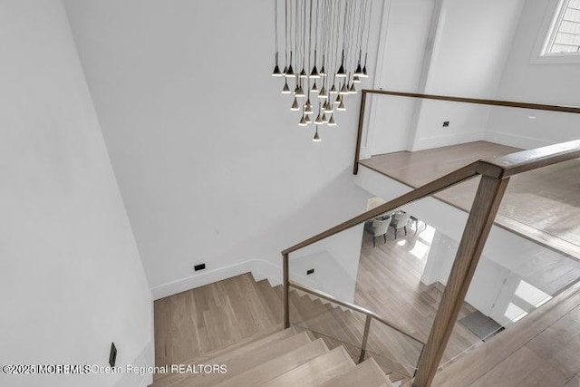 stairway with a chandelier, wood finished floors, and baseboards