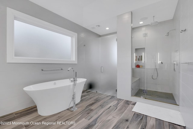 full bathroom with a stall shower, a freestanding bath, and wood finished floors