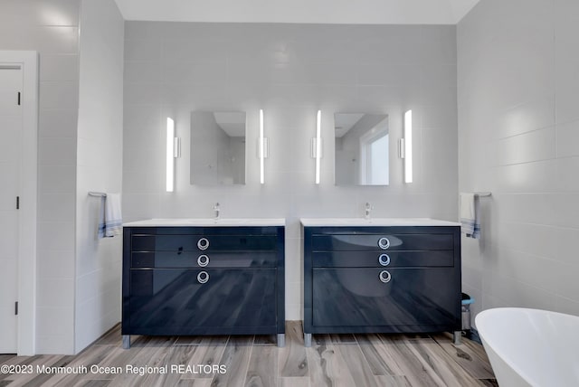 bathroom featuring tile walls, vanity, a freestanding bath, and wood finished floors