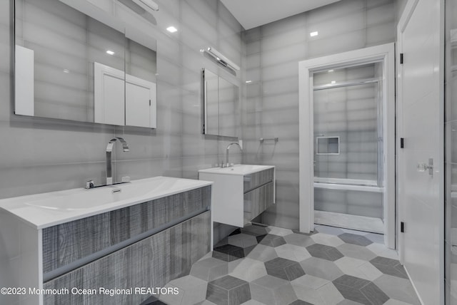 full bathroom with two vanities, tile walls, a shower with door, and tile patterned floors