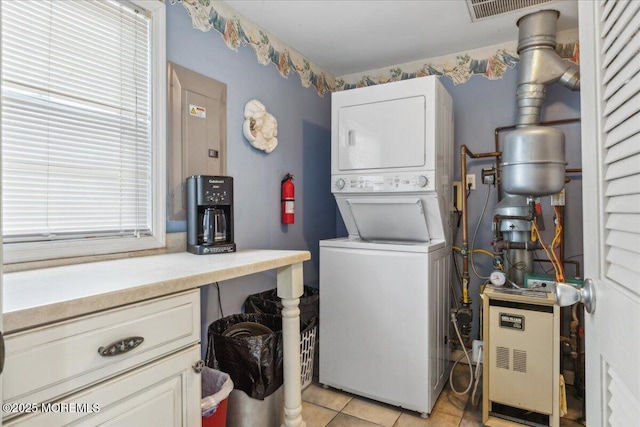 clothes washing area with estacked washer and dryer, light tile patterned floors, and a heating unit