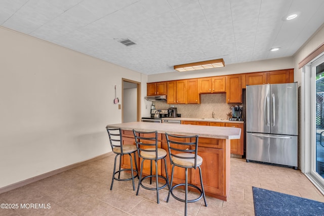 kitchen with stainless steel appliances, light countertops, under cabinet range hood, a sink, and a kitchen island