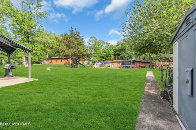 view of grassy yard featuring a playground and a patio