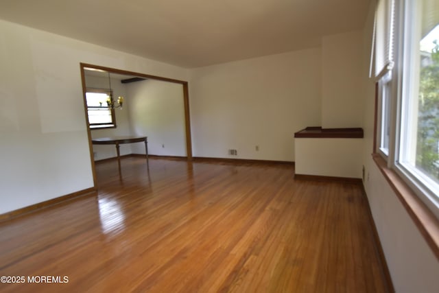 spare room featuring plenty of natural light, light wood finished floors, a chandelier, and baseboards