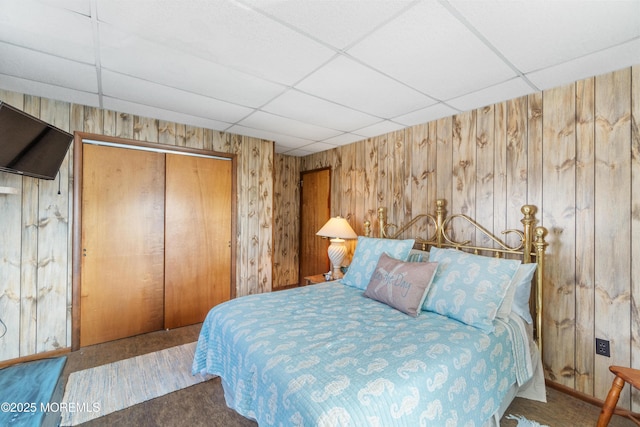 carpeted bedroom featuring a paneled ceiling, a closet, wooden walls, and baseboards