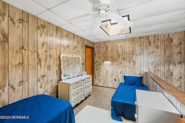 bedroom featuring a drop ceiling, wood walls, carpet flooring, and a ceiling fan