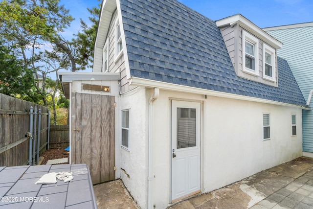 view of side of home with a shingled roof, fence, stucco siding, and a patio