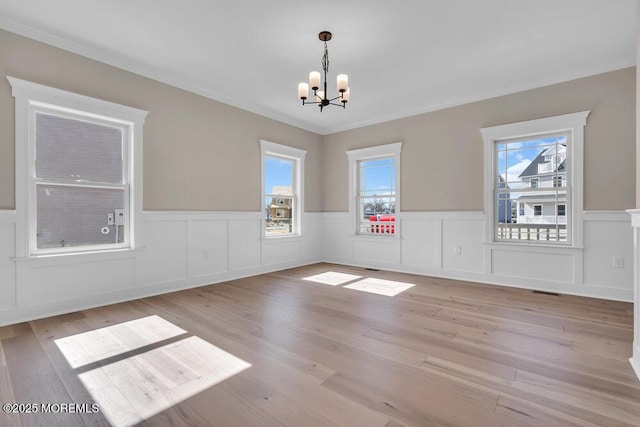 unfurnished dining area with a chandelier, light wood-type flooring, a wainscoted wall, a decorative wall, and ornamental molding