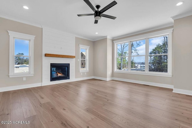unfurnished living room with crown molding, ceiling fan, baseboards, a large fireplace, and light wood finished floors