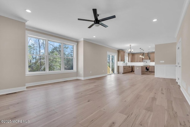 unfurnished living room featuring ornamental molding, ceiling fan, light wood finished floors, recessed lighting, and a chandelier