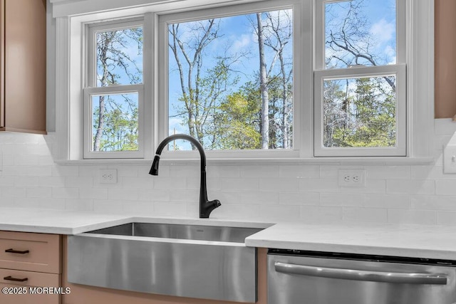 kitchen view of stainless steel dishwasher, a sink, light countertops, and tasteful backsplash