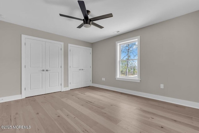 unfurnished bedroom featuring two closets, baseboards, light wood-type flooring, and ceiling fan