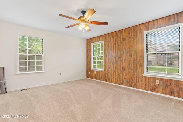 carpeted spare room featuring baseboards, wooden walls, and a ceiling fan