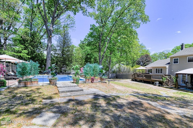 view of yard with a deck, a pool, fence, and view of scattered trees