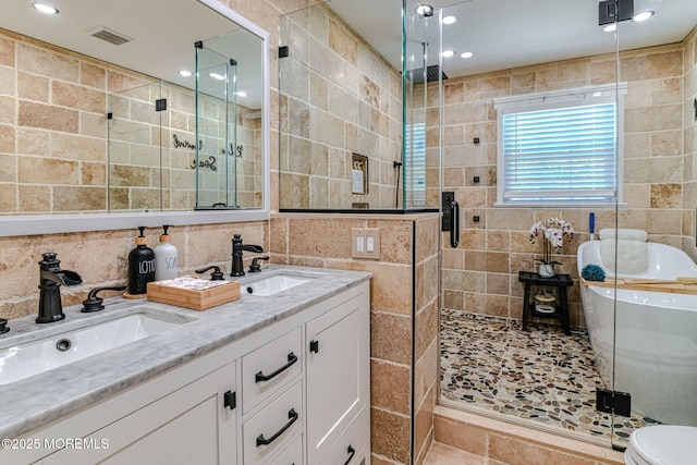 bathroom featuring tile walls, a shower stall, a freestanding bath, double vanity, and recessed lighting