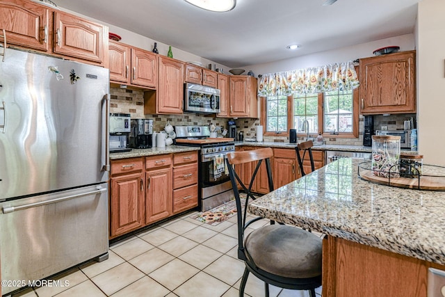 kitchen featuring stainless steel appliances, a kitchen breakfast bar, backsplash, light tile patterned flooring, and brown cabinets