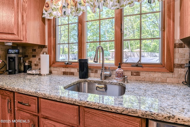 kitchen with a sink, tasteful backsplash, light stone counters, and brown cabinetry
