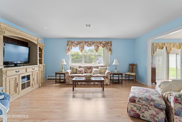 living area with baseboard heating, light wood-style flooring, a baseboard heating unit, and baseboards