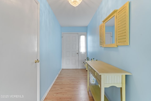 doorway to outside with light wood-style flooring, a chandelier, and baseboards