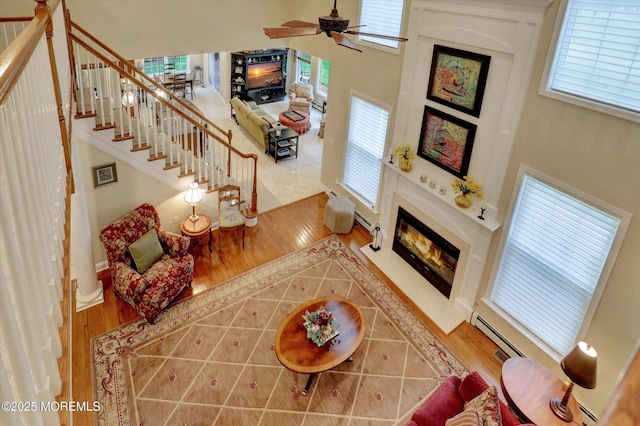 50 Hedgerow Ln, Manalapan, NJ 07726 - living area featuring a fireplace with flush hearth, wood finished floors, ceiling fan, a towering ceiling, and a baseboard radiator