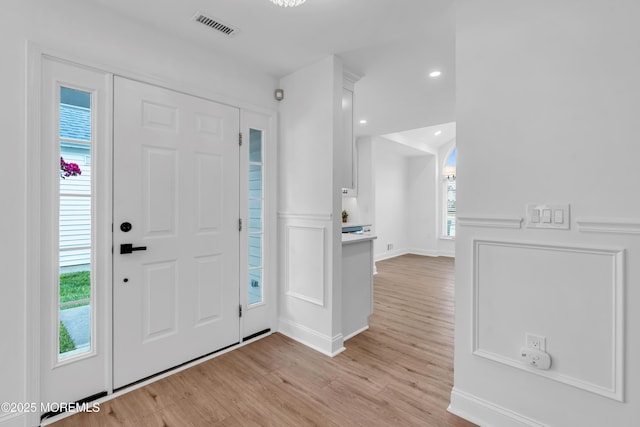 entryway with light wood finished floors, wainscoting, recessed lighting, and a decorative wall