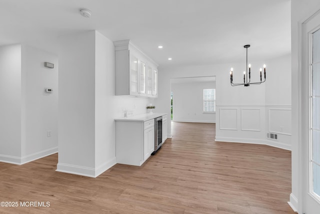 kitchen with a chandelier, wine cooler, light wood finished floors, light countertops, and white cabinets