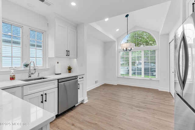kitchen featuring appliances with stainless steel finishes, a sink, light countertops, light wood-type flooring, and lofted ceiling